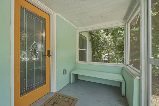 Charming screened porch with built-in bench and decorative entry door at Fruit Tree Home