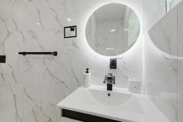 Modern marble bathroom with backlit mirror and sleek black accents at Amelia’s Arena Retreat