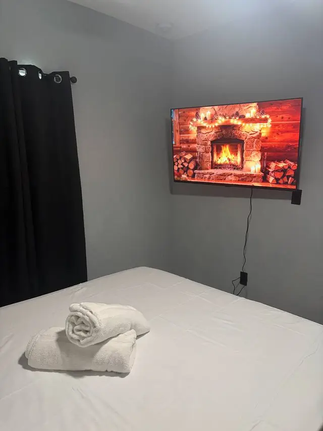 Cozy bedroom with TV, fresh towels, and dark curtains for restful stays at Amelia’s Arena Retreat