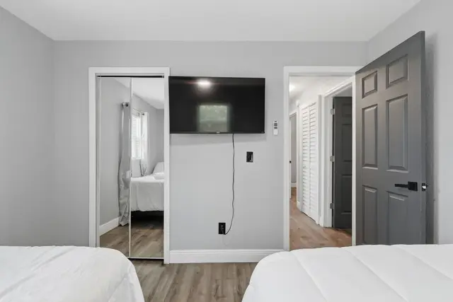 Bright modern bedroom with two beds, TV, and mirrored closet at WinterPark Home