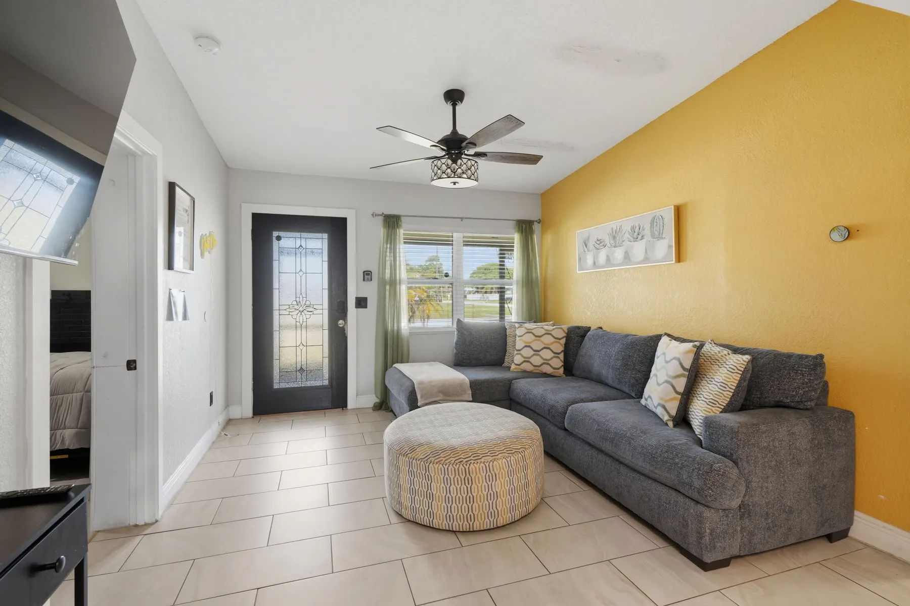Bright living room with cozy sectional, sunny accent wall, and natural light at The Clue House, a Libema home in Orlando