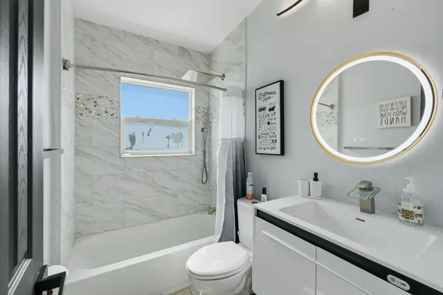 Bright modern bath with marble tile, tub-shower, and LED mirror at The Clue House