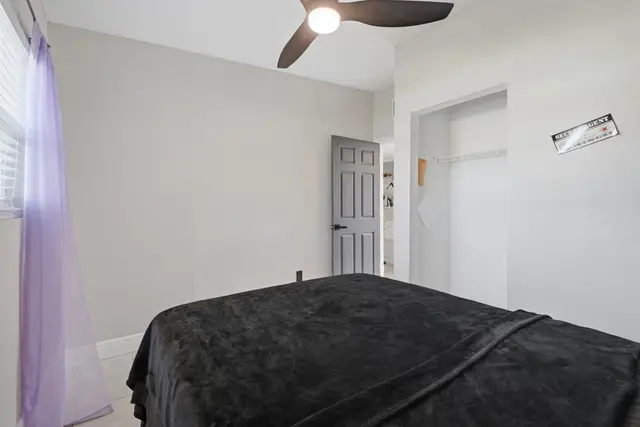 Bright, minimalist bedroom with ceiling fan and open closet space at The Clue House