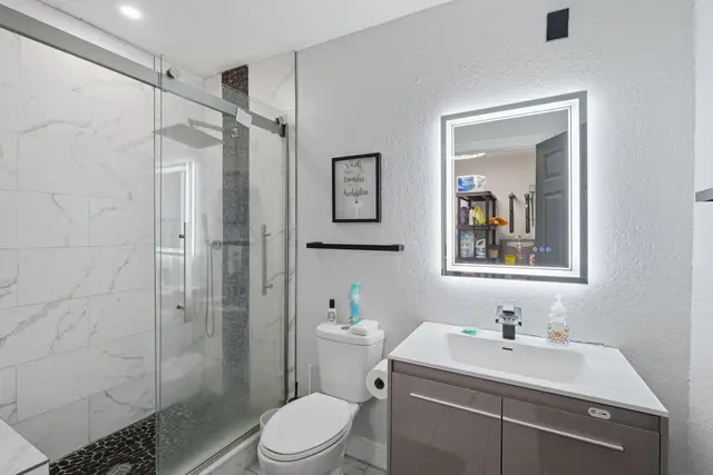 Modern spa-style bathroom with glass shower and illuminated mirror at The Clue House
