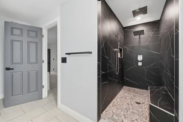 Spa-like walk-in shower with dual rainfall heads and luxe modern finishes at The Clue House