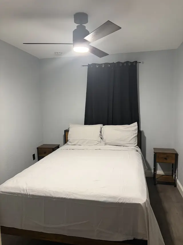 Cozy queen room with blackout curtains, modern fan, and rustic nightstands. at Downtown & Stadium Cozy Retreat