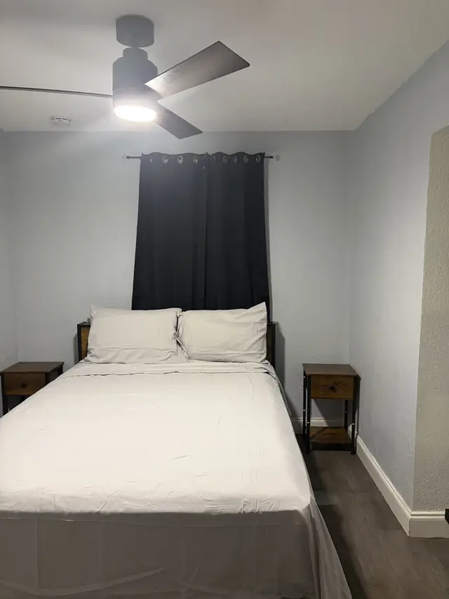 Cozy minimalist room with queen bed, blackout drapes, fan, and dual nightstands at Downtown & Stadium Cozy Retreat