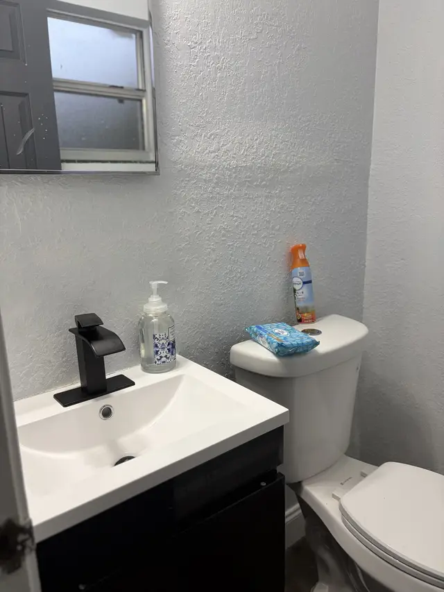 Modern, compact bath with sleek vanity, frosted window, and essentials at Downtown & Stadium Cozy Retreat
