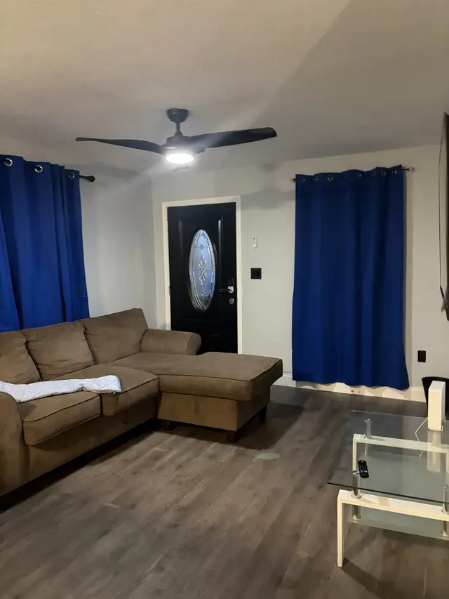 Cozy living area with sectional, sleek fan, bold blue drapes, glass table at Downtown & Stadium Cozy Retreat