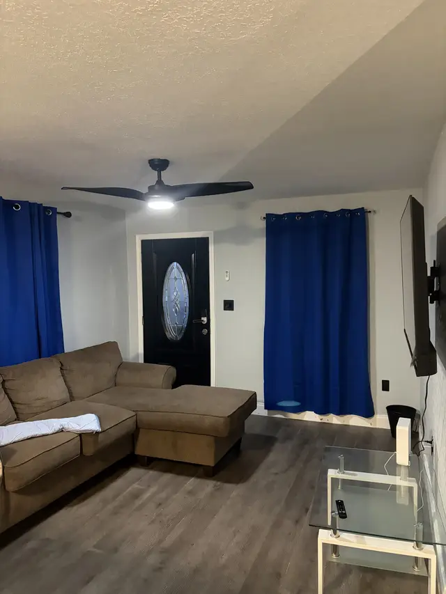 Cozy lounge with sectional, wall-mounted TV, and blue accents. at Downtown & Stadium Cozy Retreat