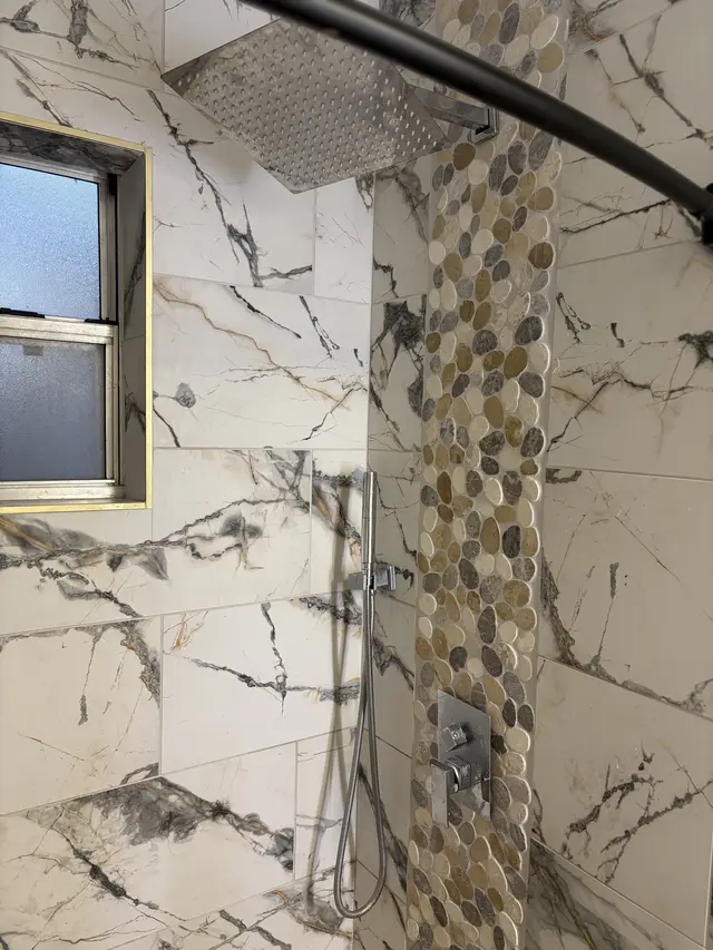Spa-like shower with rainfall head, pebble accent, and marble-look tile. at Downtown & Stadium Cozy Retreat