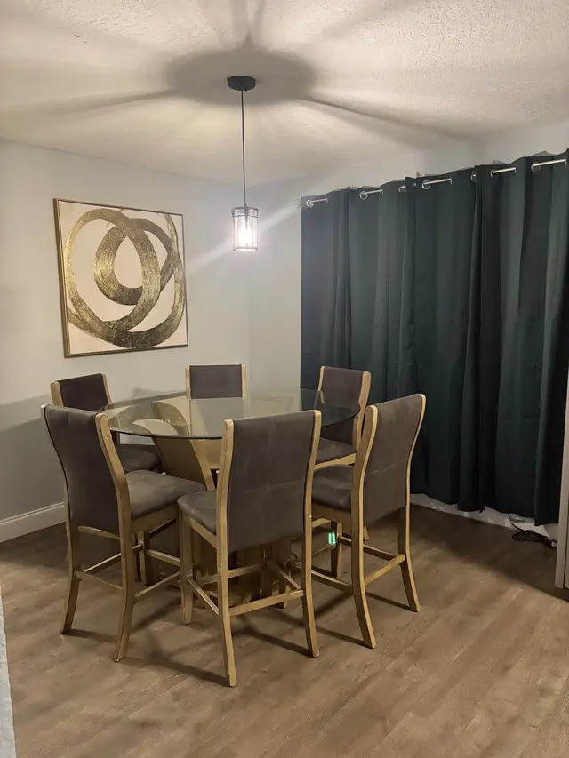 Modern dining nook with glass table, plush chairs, moody drapes, pendant light at Downtown & Stadium Cozy Retreat